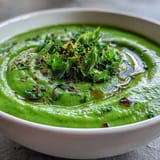 Vibrant green detox vegetable soup with zucchini, peas, and spinach in a creamy puree, garnished with fresh herbs and lemon zest.