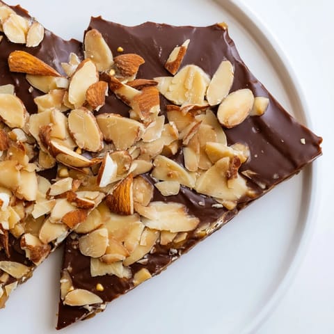 A close-up of buttery English toffee, glistening with melted milk chocolate and crunchy almonds.
