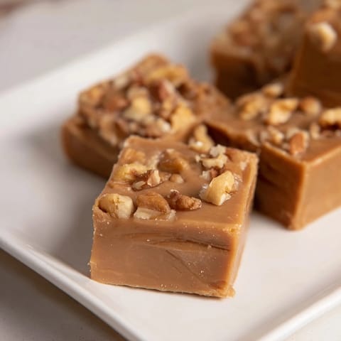 Warm, caramel-colored Penuche Fudge squares glistening, promising a rich, melt-in-your-mouth flavor.