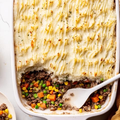 Bubbling Shepherd’s Pie casserole fresh from the oven, featuring fluffy ridged potatoes topping a rich ground beef, carrot, and pea mixture.