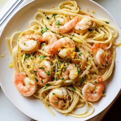 Plump shrimp and al dente linguine glisten in a rich garlic butter sauce, with a lemon wedge and Parmesan nearby.