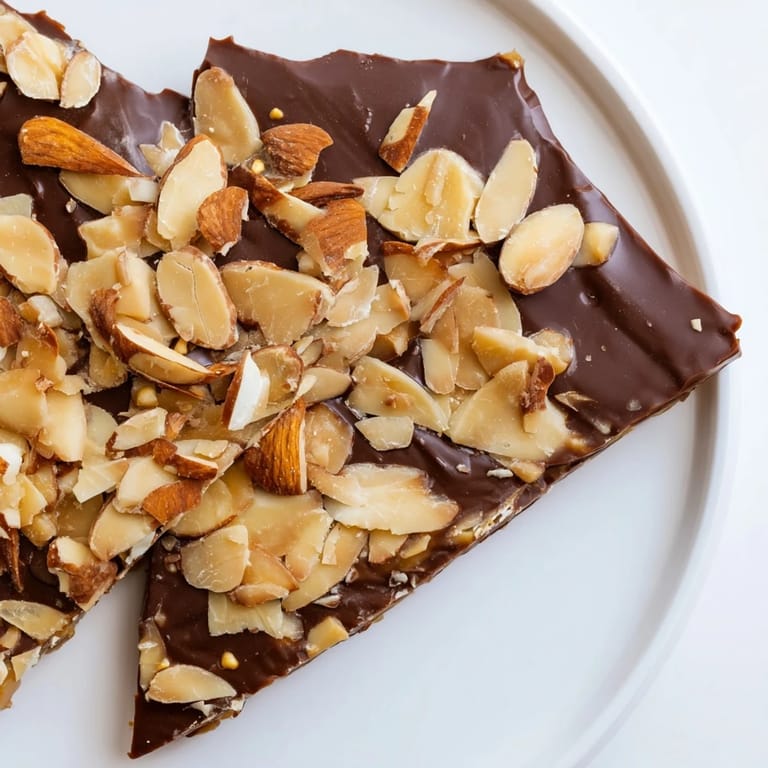 A close-up of buttery English toffee, glistening with melted milk chocolate and crunchy almonds.