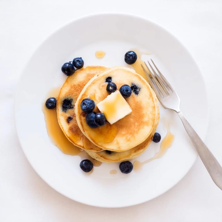 A rustic stack of blueberry pancakes topped with more berries and a dusting of powdered sugar.