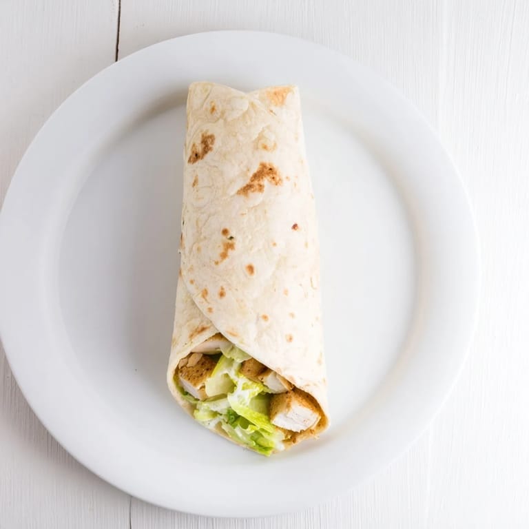 Freshly made Caesar Chicken Salad Wrap cut in half, revealing layers of grilled chicken, romaine, and parmesan cheese.