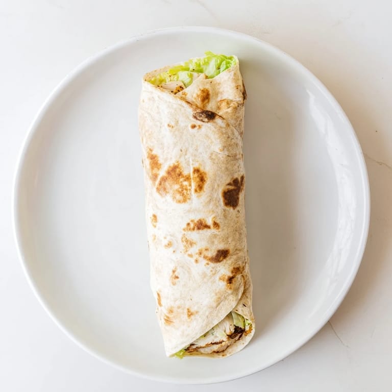 Sliced Caesar Chicken Salad Wrap showing juicy grilled chicken, chopped lettuce, parmesan, and crunchy croutons inside a flour tortilla.  