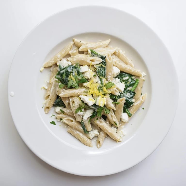 Close-up of Creamy Feta Spinach Pasta showing vibrant spinach leaves and feta pieces coating penne, steaming in a skillet for a comforting meal.